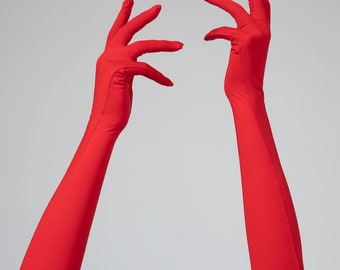 Puede incluir: Un par de guantes largos de color rojo con los dedos extendidos. Los guantes están hechos de un tejido liso y elástico.