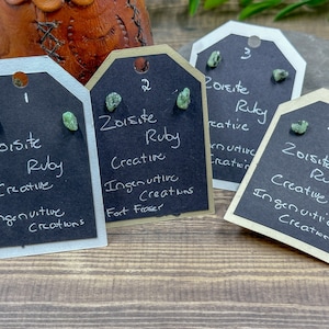 Peut inclure: Quatre petites cartes avec un fond noir et du texte blanc. Chaque carte a une paire de boucles d'oreilles en rubis zoïsite vertes et le texte "Zoisite Ruby", "Creative", "Ingenuitive Creations", et un numéro de 1 à 4.