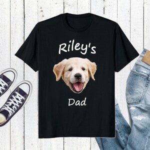 May include: Black t-shirt with a white graphic of a golden retriever puppy. The text "Riley's Dad" is printed below the puppy.