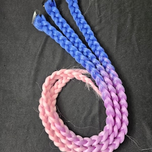 May include: Three blue braided hair extensions with metal clips, and a pink to purple braided hair extension. The hair extensions are arranged on a black surface. The braids are tightly woven and show a gradient of colors.