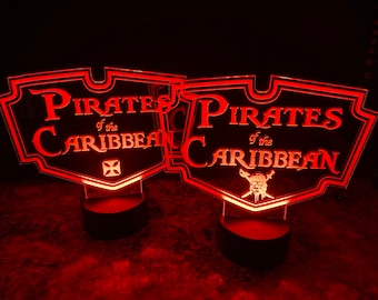 May include: Two red illuminated signs with the text "Pirates of the Caribbean" in white. One sign features a skull and crossbones, while the other has a black cross.