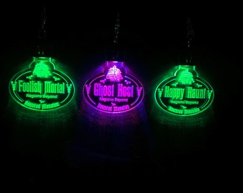 May include: Three glowing green, purple, and green light-up ornaments with the text "Foolish Mortal", "Ghost Host", and "Happy Haunt" on them. Each ornament has the text "Regions Beyond" and "Haunted Mansion" on them.