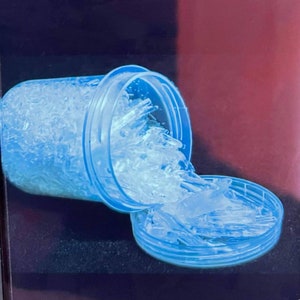 May include: A clear plastic container with a blue lid is overflowing with white crystals. The container is tipped over, and the crystals are spilling out onto a blue surface.