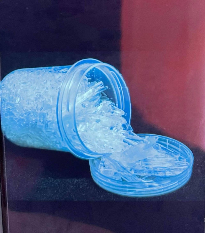 May include: A clear plastic container with a blue lid is overflowing with white crystals. The container is tipped over, and the crystals are spilling out onto a blue surface.