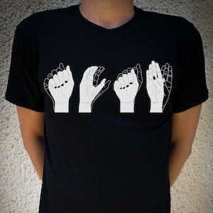 Può includere: Una maglietta nera con una grafica bianca di cinque mani che firmano la parola "LOVE" nel linguaggio dei segni americano.