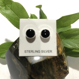 May include: A pair of black onyx stud earrings with sterling silver posts. The earrings are displayed on a white card with the words "Sterling Silver" printed on it.