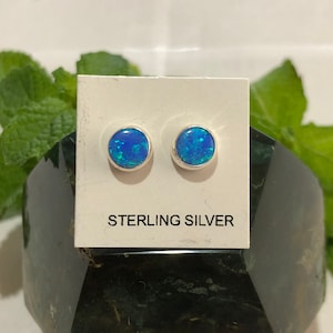 May include: A pair of sterling silver stud earrings with blue opal stones. The earrings are displayed on a white card with the text "STERLING SILVER".