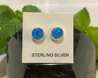 May include: A pair of sterling silver stud earrings with blue opal stones. The earrings are displayed on a white card with the text "STERLING SILVER".