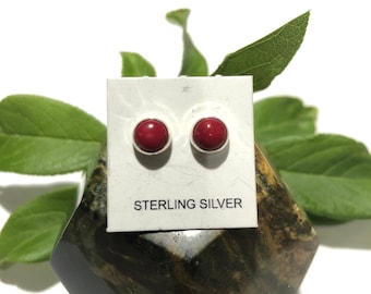 May include: A pair of red gemstone stud earrings with sterling silver settings. The earrings are displayed on a white card with the words "Sterling Silver" printed on it.