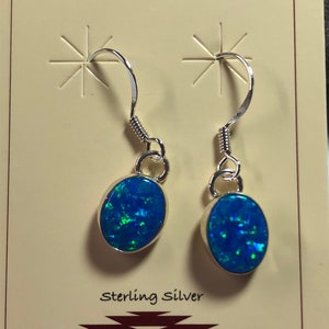 May include: A pair of sterling silver earrings with blue opal stones. The earrings have a simple design with a small oval-shaped stone hanging from a silver hook.
