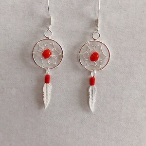 May include: A pair of silver dreamcatcher earrings with red beads and silver feathers.