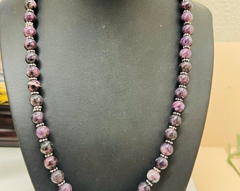 May include: A purple and silver beaded necklace with a silver clasp. The beads are round and have a marbled pattern.