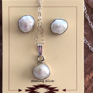 May include: A set of pearl earrings and a pearl necklace with a sterling silver chain. The pearls are white and have an iridescent sheen. The necklace and earrings are displayed on a brown card with the text "Sterling Silver".