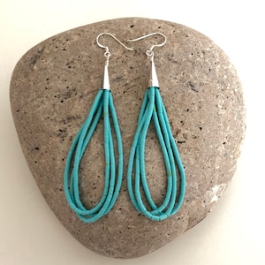 May include: A pair of long turquoise dangle earrings with silver hooks. The earrings are made of multiple strands of turquoise beads.