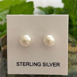 May include: A pair of white pearl stud earrings on a white card with the text "STERLING SILVER".