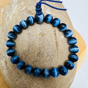 May include: A blue and white tiger's eye beaded bracelet with a dark blue cord and tassel.