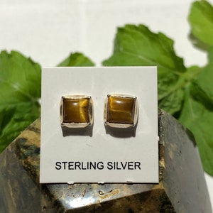 May include: A pair of sterling silver earrings with square-shaped tiger's eye gemstones. The earrings are on a white card with the text "STERLING SILVER".