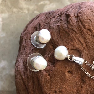 May include: A set of pearl earrings and a pearl pendant necklace. The pearls are white and have a slightly irregular shape. The earrings are silver and have a post back. The necklace is silver and has a chain with a lobster clasp.