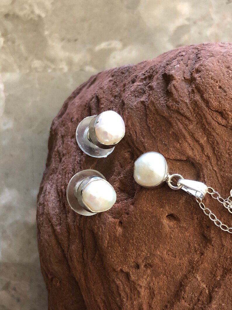 May include: A set of pearl earrings and a pearl pendant necklace. The pearls are white and have a slightly irregular shape. The earrings are silver and have a post back. The necklace is silver and has a chain with a lobster clasp.