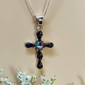 May include: A silver chain necklace with a purple and turquoise inlay cross pendant. The cross is made of sterling silver and features a variety of stones, including turquoise, red coral, and white mother of pearl.