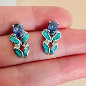 May include: A pair of silver earrings with blue and green opal stones. The earrings feature a delicate, intricate design.