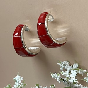 May include: A pair of red and silver hoop earrings. The earrings are made of silver and have a red enamel inlay. The earrings are a simple and elegant design.