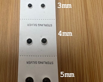 May include: Three pairs of black stud earrings in sterling silver. The earrings are displayed on a white card with the size of each pair listed: 3mm, 4mm, and 5mm.