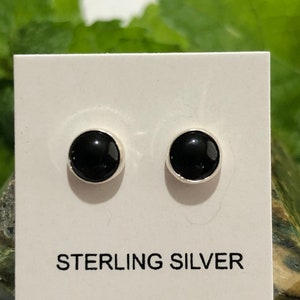 May include: A pair of black onyx stud earrings set in sterling silver. The earrings are displayed on a white card with the text "STERLING SILVER".