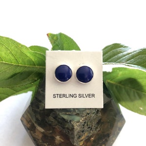 May include: A pair of sterling silver stud earrings with round blue stones. The earrings are displayed on a white card with the text "STERLING SILVER".
