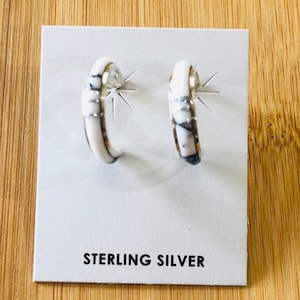 May include: A pair of sterling silver hoop earrings with a white marble design. The earrings are displayed on a white card with the text "STERLING SILVER".