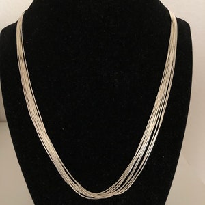 May include: A silver chain necklace with multiple strands, displayed on a black mannequin bust.
