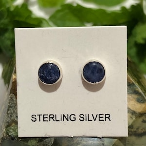 May include: A pair of sterling silver stud earrings with round blue gemstone accents. The earrings are displayed on a white card with the text "STERLING SILVER".