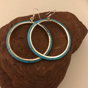 May include: A pair of silver hoop earrings with a turquoise inlay. The earrings are round and have a simple design.
