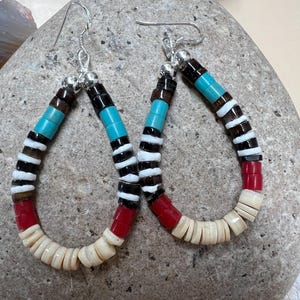 May include: A pair of dangle earrings with a teardrop shape. The earrings are made with a variety of colorful beads, including red, white, black, brown, and turquoise. The beads are strung on a silver wire and have a silver hook closure.
