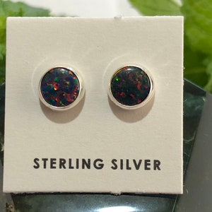 May include: A pair of sterling silver stud earrings with black opal stones. The earrings are on a white card with the text "STERLING SILVER" printed on it.