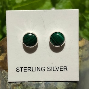 May include: A pair of sterling silver earrings with round green malachite stones. The earrings are displayed on a white card with the text "STERLING SILVER".