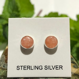 May include: A pair of sterling silver stud earrings with pink and white speckled stone accents. The earrings are displayed on a white card with the text "STERLING SILVER".