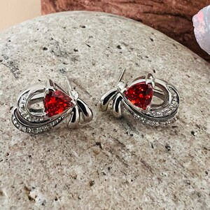 May include: A pair of silver earrings with red gemstone accents. The earrings feature a delicate, swirling design with small clear stones.