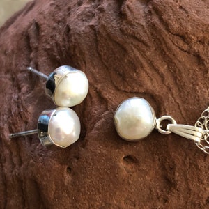 May include: A set of pearl jewelry featuring a pendant necklace and a pair of stud earrings. The pearls are white and have an irregular shape. The jewelry is made of silver.