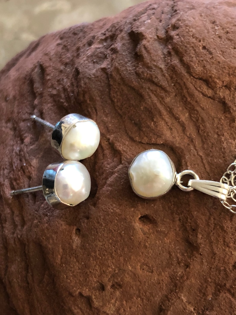 May include: A set of pearl jewelry featuring a pendant necklace and a pair of stud earrings. The pearls are white and have an irregular shape. The jewelry is made of silver.