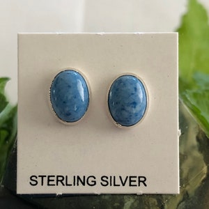 May include: A pair of sterling silver stud earrings with blue oval-shaped stones. The earrings are displayed on a white card with the text "STERLING SILVER".
