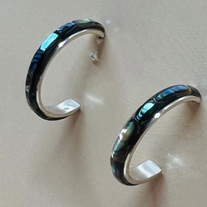 May include: A pair of silver hoop earrings with a black and iridescent abalone shell inlay.