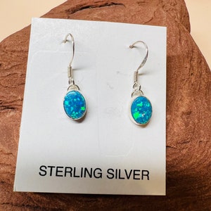 May include: A pair of sterling silver earrings with oval-shaped blue opal stones. The earrings are on a white card with the text "STERLING SILVER".