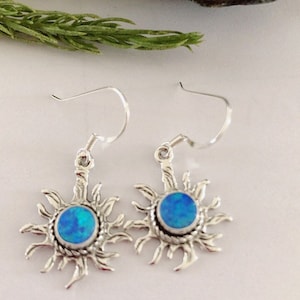 May include: A pair of silver earrings with blue opal stones set in a sunburst design.