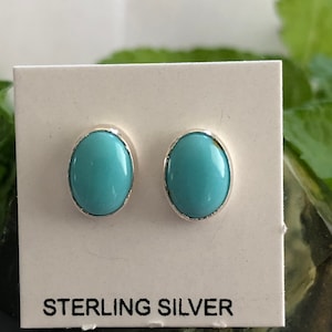 May include: A pair of sterling silver earrings with oval-shaped turquoise stones. The earrings are displayed on a white card with the words "Sterling Silver" printed on it.
