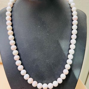 May include: A white and pink coral bead necklace. The necklace is made of round beads and is strung on a white cord.