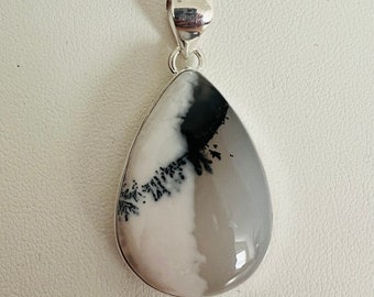 May include: A silver chain necklace with a teardrop-shaped pendant featuring a white and black dendritic agate stone.