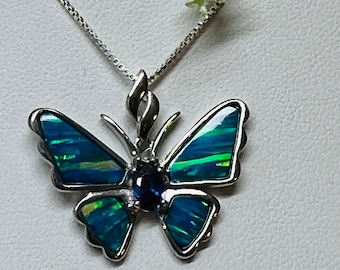 May include: A silver butterfly pendant necklace with a blue opal stone. The butterfly wings are iridescent and have a green and blue color.