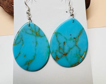 May include: A pair of turquoise dangle earrings with gold veining. The earrings are oval shaped and have silver hooks.