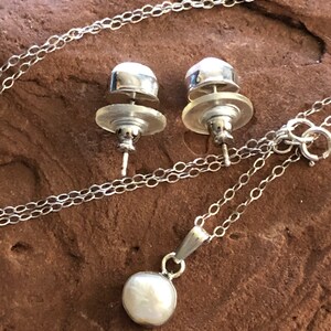 May include: A silver necklace with a pearl pendant and matching pearl stud earrings. The necklace has a delicate chain and the pearl pendant is round and white.
